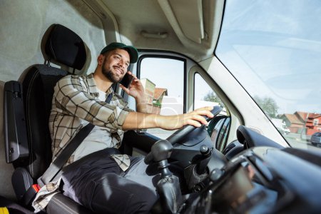 Téléchargez les photos : Jeune beau livreur parle au téléphone tout en conduisant un camion - en image libre de droit