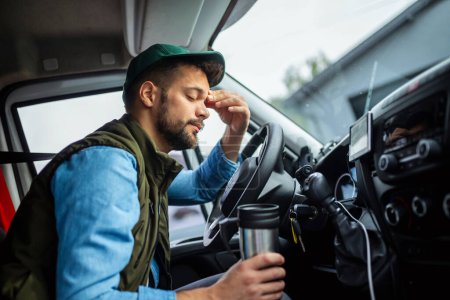 Foto de Conductor de camión cansado sosteniendo café en su cabina. - Imagen libre de derechos