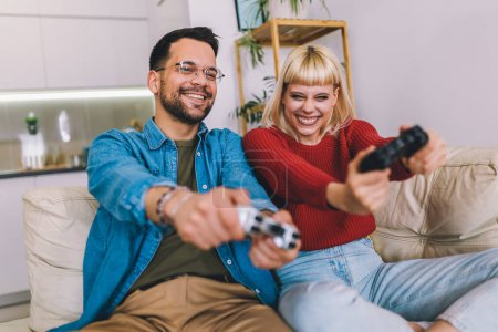 Photo for Boyfriend and girlfriend playing video game with joysticks in living room. Loving couple are playing video games at home - Royalty Free Image