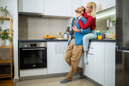 Téléchargez les photos : Jeune homme et jeune femme debout dans la cuisine et parlant. Heureuse épouse et mari avec des tasses de café et de jus debout dans la cuisine. - en image libre de droit