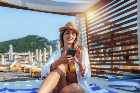 Téléchargez les photos : Jeune belle femme utilisant son téléphone tout en se refroidissant sur la plage. - en image libre de droit