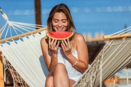 Photo for Young beautiful woman eating juicy watermelon on the beach. - Royalty Free Image