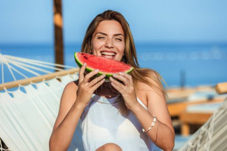 Photo for Young beautiful woman eating juicy watermelon on the beach. - Royalty Free Image