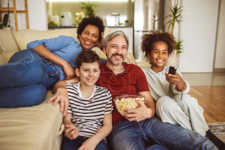 Photo for Young family watching TV together at home and having fun together. - Royalty Free Image