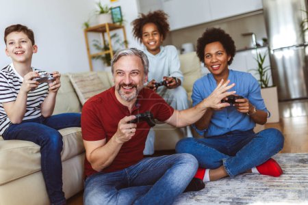 Téléchargez les photos : Smiling family enjoying time together at home sitting on sofa in living room and playing video games. - en image libre de droit
