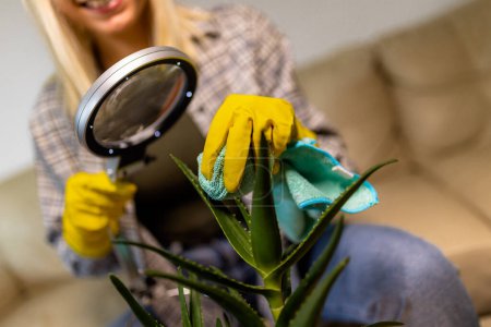 Téléchargez les photos : Jeune femme blonde prenant soin de ses plantes. Utilisation de loupe - en image libre de droit
