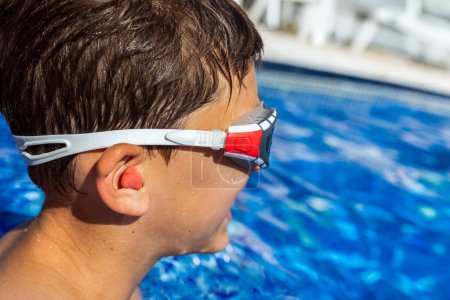 Foto de Niño preparándose para nadar en la piscina, teniendo tapones para los oídos y gafas. Vacaciones de verano. - Imagen libre de derechos