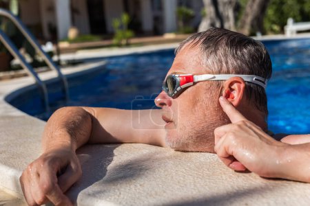 Téléchargez les photos : Homme d'âge moyen mettre des bouchons d'oreille avant de nager dans la piscine - en image libre de droit