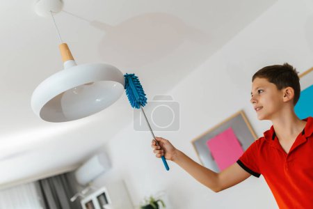 Foto de Niño varón limpiando la lámpara. Haciendo sus tareas. - Imagen libre de derechos