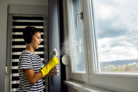 Téléchargez les photos : Homme enfant nettoyer la fenêtre avec le spray et porter le casque tout en écoutant la musique - en image libre de droit