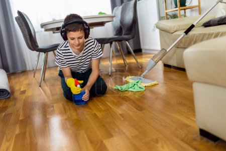 Foto de Niño varón limpiando el suelo con tela mientras usa los auriculares y escucha la música - Imagen libre de derechos