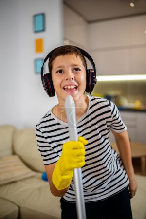 Téléchargez les photos : Un garçon qui nettoie le sol et écoute de la musique. Il fait sa corvée et il danse - en image libre de droit