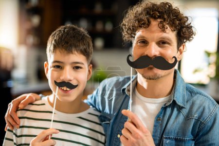 Téléchargez les photos : Papa et fils tenant une fausse moustache. Prévention du cancer de la prostate - en image libre de droit