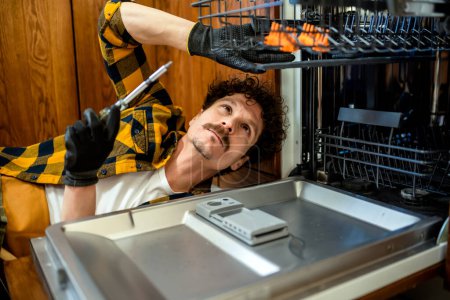 Photo for Latino man fixing dishwasher in the kitchen. - Royalty Free Image