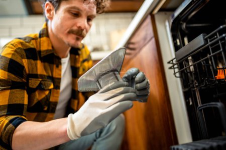 Foto de Hombre latino arreglando lavavajillas en la cocina. - Imagen libre de derechos