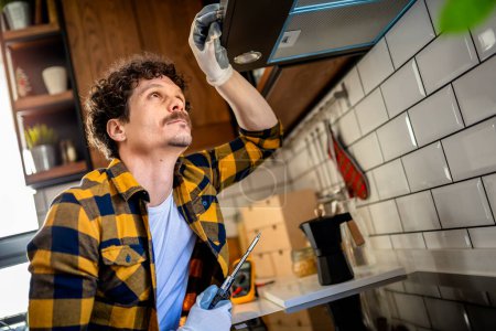 Téléchargez les photos : Latino homme fixation aspirateur dans la cuisine. - en image libre de droit