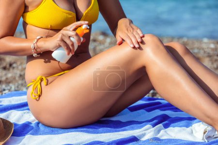 Foto de Hermosa joven poniéndose protector solar en la playa. - Imagen libre de derechos