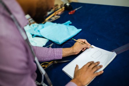 Téléchargez les photos : Homme afro-américain tailleur fait un croquis dans son atelier. - en image libre de droit
