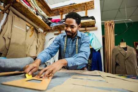 Photo for Young African American tailor drawing with chalk on material in his own atelier. - Royalty Free Image