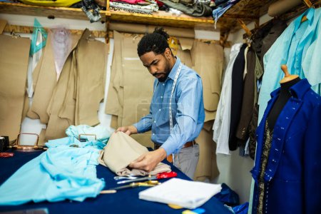 Photo for Young African American tailor choosing fabric in his own atelier. - Royalty Free Image