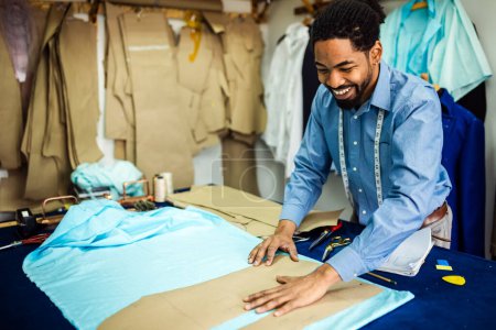 Téléchargez les photos : Jeune tailleur afro-américain choisissant le tissu dans son propre atelier. - en image libre de droit