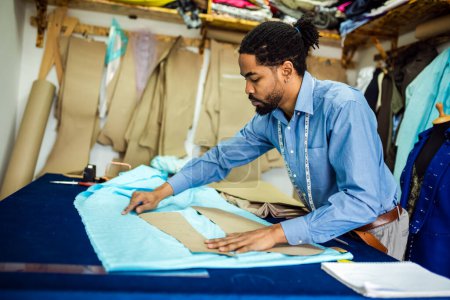 Photo for Young African American tailor drawing with chalk on material in his own atelier. - Royalty Free Image