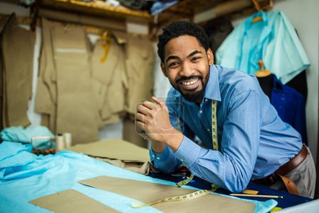Téléchargez les photos : Jeune tailleur afro-américain souriant dans son propre atelier. - en image libre de droit