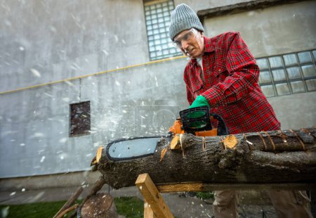 Téléchargez les photos : Homme coupant du bois avec scie, poussière et mouvements. Tronçonneuse
. - en image libre de droit