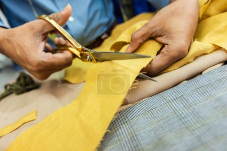 Téléchargez les photos : Jeune tailleur afro-américain coupe avec des ciseaux tissu jaune dans son propre atelier. - en image libre de droit