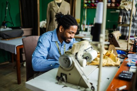 Photo for Young male African American tailor sew with a sewing machine in his own atelier - Royalty Free Image