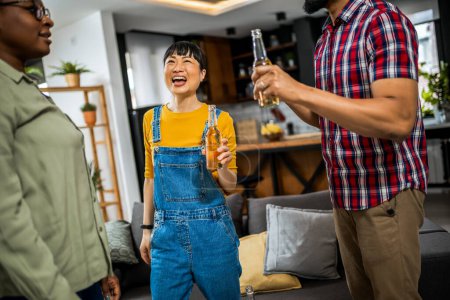 Téléchargez les photos : Groupe multiethnique d'amis à la maison dansant et chantant avec de la bière dans leurs mains. - en image libre de droit