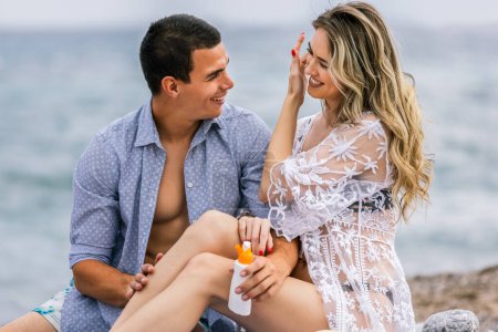 Photo for Young couple on the beach applying the tanning cream - Royalty Free Image