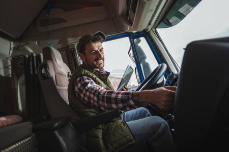 Foto de Feliz conductor varón confiado sentado en su camión, usando su tableta - Imagen libre de derechos