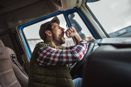 Téléchargez les photos : Un conducteur de camion fatigué prend une pause de la conduite et se repose dans son camion - en image libre de droit