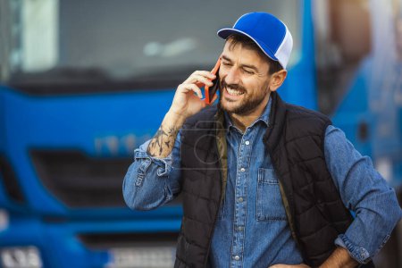 Téléchargez les photos : Conducteur masculin confiant heureux debout devant son camion, utilisant son téléphone pour parler à quelqu'un - en image libre de droit
