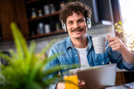 Photo for Latino man wearing headphones and talking to someone while drinking a hot beverage - Royalty Free Image