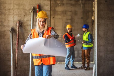 Photo for Female architect with helmet and safety jacket on construction site examining office blueprints. - Royalty Free Image