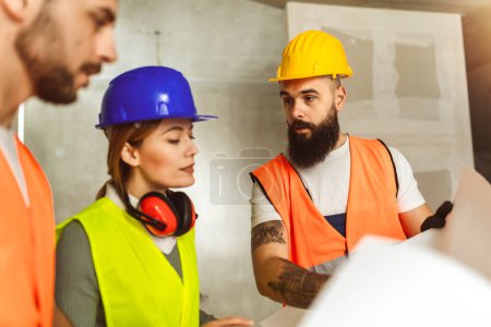 Foto de Equipo de construcción con cascos y chaleco de seguridad en obra examinando planos de oficinas. - Imagen libre de derechos