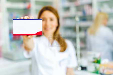 Téléchargez les photos : Une pharmacienne tenant une boîte de médicaments dans la pharmacie. - en image libre de droit
