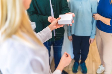 Photo for Cheerful pharmacist chemist woman giving vitamins to young family of three in modern pharmacy. - Royalty Free Image