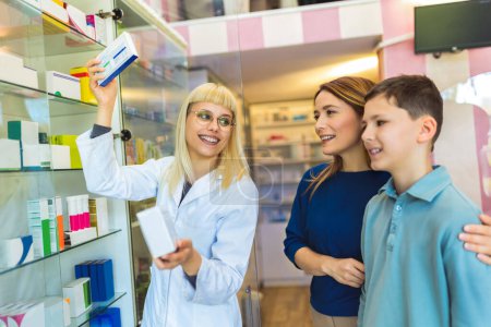 Photo for Cheerful pharmacist chemist woman giving vitamins to young mom with son in modern pharmacy. - Royalty Free Image