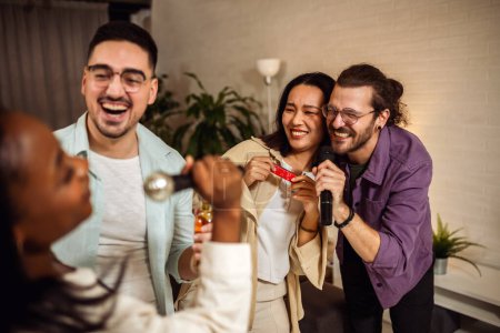 Téléchargez les photos : Groupe multiracial d'amis ayant nuit karaoké. Chanter au micro, boire de la bière et jouer de l'orgue. - en image libre de droit
