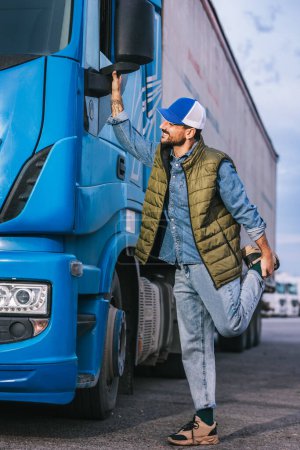 Téléchargez les photos : Conducteur masculin fatigué debout devant son camion et se traînant après une longue route - en image libre de droit