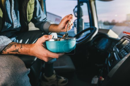 Photo for Truck driver taking a break from long drive to eat some food from container. - Royalty Free Image