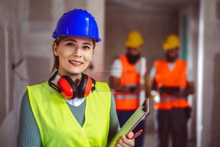 Photo for Portrait of successful woman constructor wearing yellow helmet and safety yellow vest. Portrait of architect standing at building site and looking at camera. - Royalty Free Image