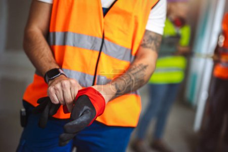 Téléchargez les photos : Travailleur de la construction met des gants sur un chantier de construction. - en image libre de droit