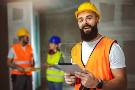 Téléchargez les photos : Gestionnaire de chantier debout portant un gilet de sécurité et un casque, tenant une tablette. - en image libre de droit
