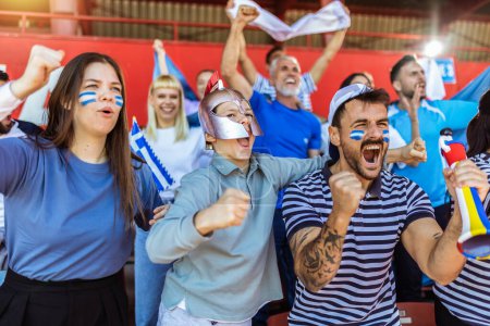 Téléchargez les photos : Les fans grecs applaudissent au match sur le stade. Porter des couleurs bleues et blanches pour soutenir leur équipe. Célébration avec drapeaux et foulards. - en image libre de droit
