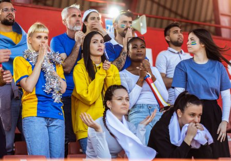 Téléchargez les photos : Les fans de sport applaudissent au match sur le stade. Porter des couleurs jaunes et bleues pour soutenir leur équipe. Célébration avec drapeaux et foulards. - en image libre de droit