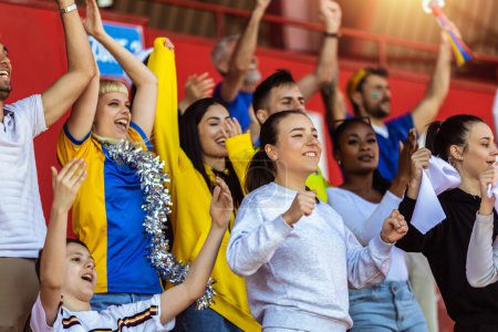 Téléchargez les photos : Les fans de sport applaudissent au match sur le stade. Porter des couleurs jaunes et bleues pour soutenir leur équipe. Célébration avec drapeaux et foulards. - en image libre de droit